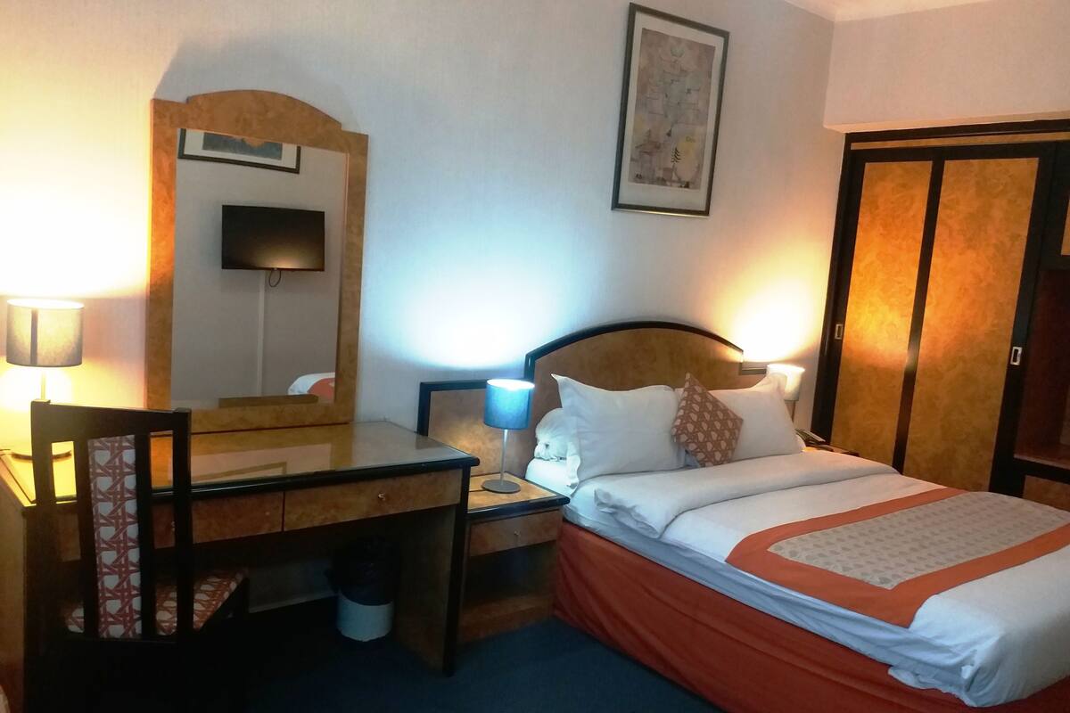 Une chambre d’hôtel équipée d’un lit, d’un bureau, d’une chaise et d’un téléviseur fixé au mur.