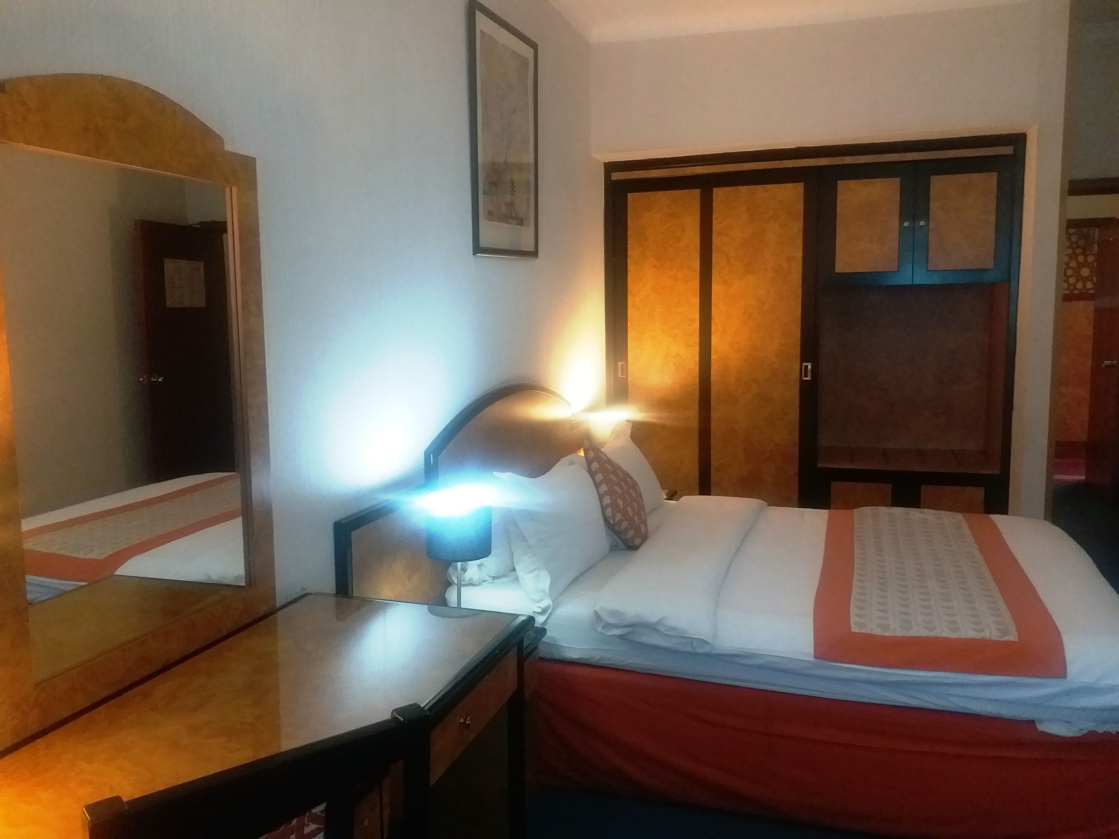 Una habitación de hotel con una cama, un escritorio, una silla, un espejo y un armario.
