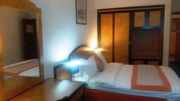 Una habitación de hotel con una cama, un escritorio, una silla, un espejo y un armario.