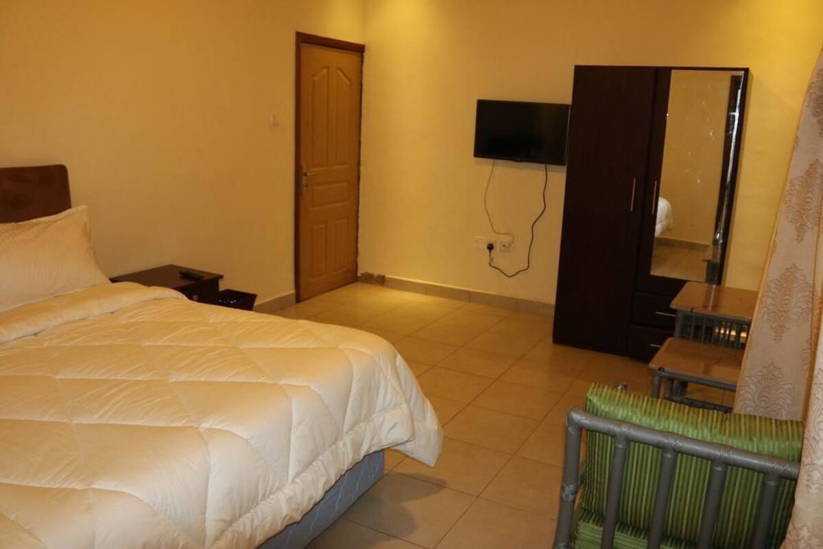 A hotel room with a bed, a television mounted on the wall, a wardrobe, and a radiator.