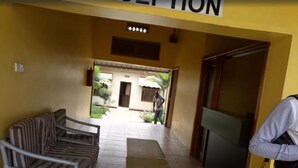 Un espace d’accueil d’hôtel comprenant un comptoir de réception, un espace d’attente avec des chaises à rayures et une vue sur l’entrée du bâtiment.