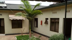 Un bâtiment doté d’un toit en tuiles, d’un patio couvert et d’un petit jardin avec un palmier.