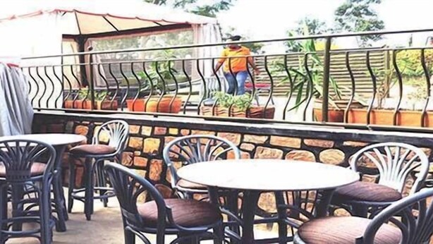 Un espace extérieur aménagé avec des chaises et des tables en métal, un mur en pierre et une personne qui s’occupe des plantes.