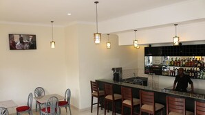 Il y a un espace bar avec un comptoir, des tabourets de bar et un barman. Un coin repas est aménagé avec une table et des chaises.