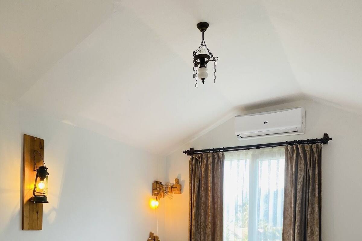 Un dormitorio con cama, suelo de madera, ventilador de techo, aire acondicionado y ventana con cortinas.