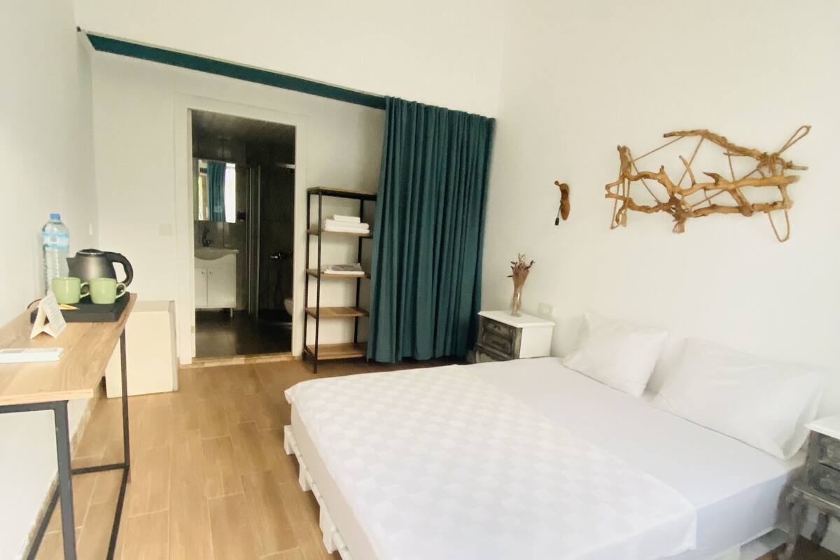 Un dormitorio con una cama, un escritorio, una silla, un estante y una puerta que da a un baño.