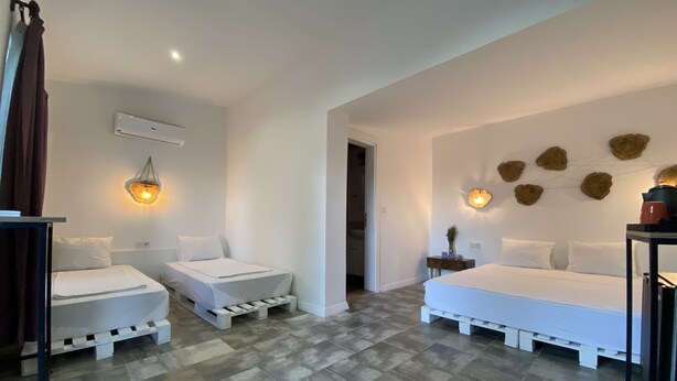 Habitación de hotel moderna con dos camas individuales, una cama grande, suelo de baldosas grises y un aplique de pared.