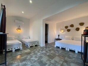 Habitación de hotel moderna con dos camas individuales, una cama grande, suelo de baldosas grises y un aplique de pared.