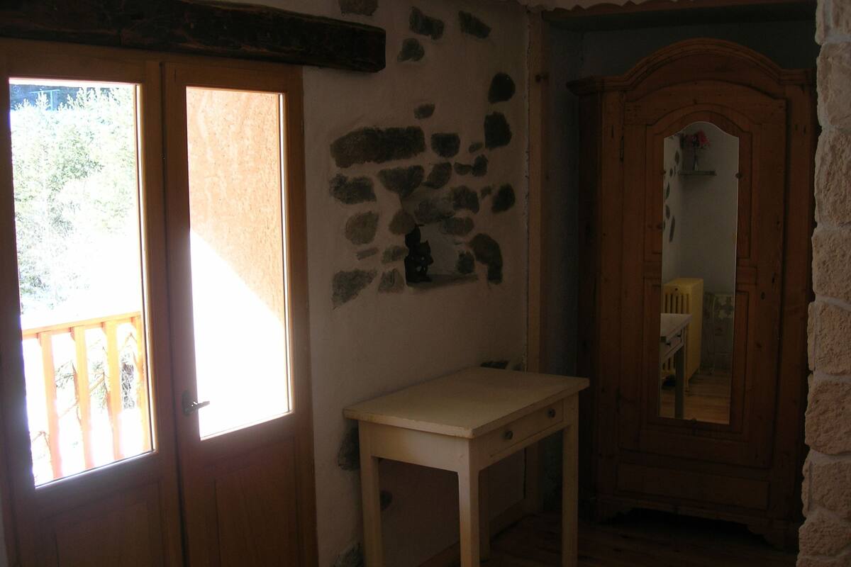 A room with a wooden door, a small table, a mirror, and a stone wall.