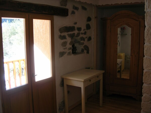 A room with a wooden door, a small table, a mirror, and a stone wall. - Auberge La Cleida (Nevache)