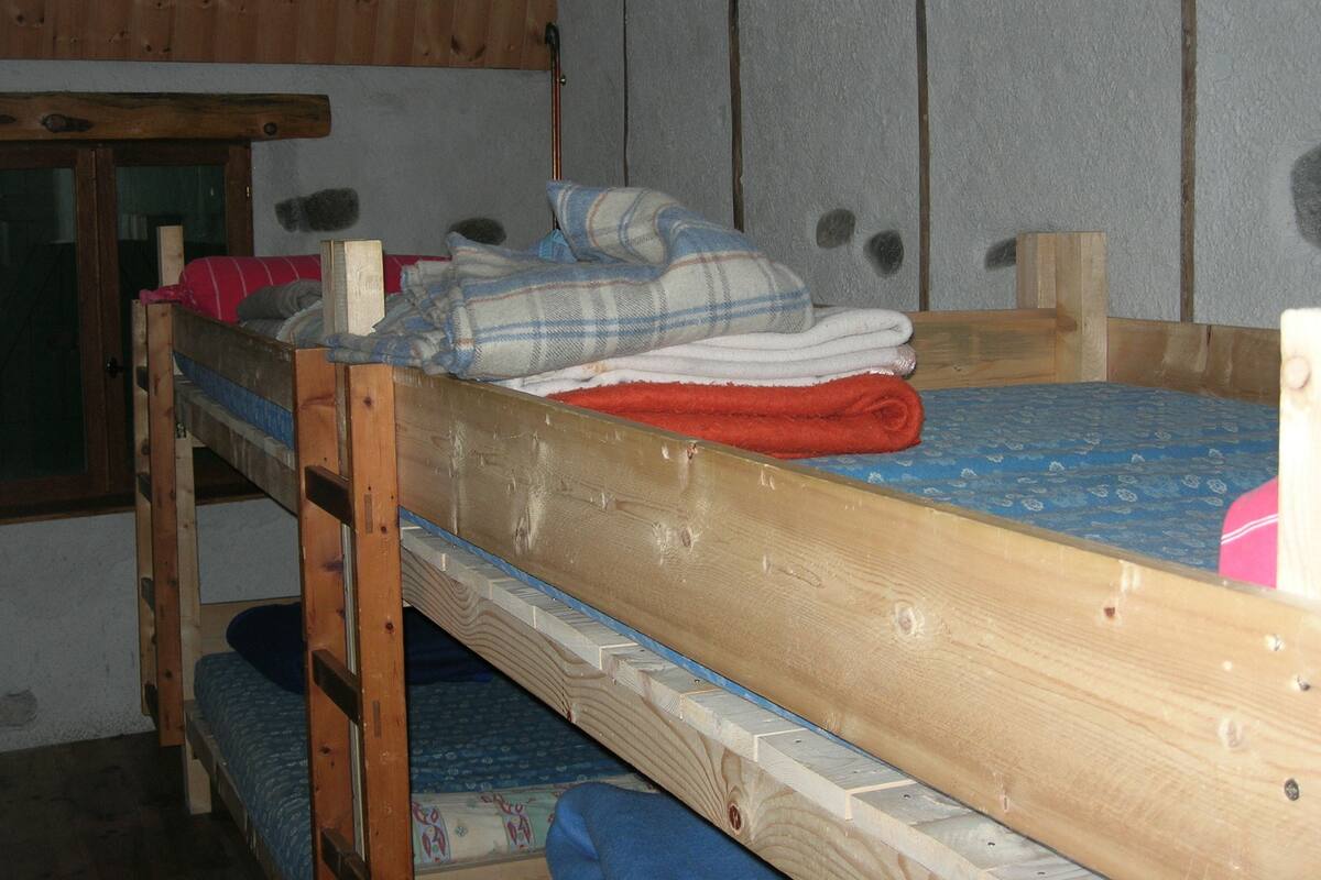 A small, compact room with a bunk bed and a single bed. The room has a simple, functional design with a window and a door.
