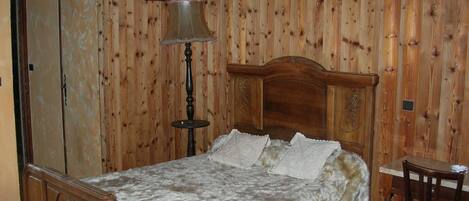 A wooden-paneled bedroom with a bed, a nightstand, a chair, and a hanging lamp.