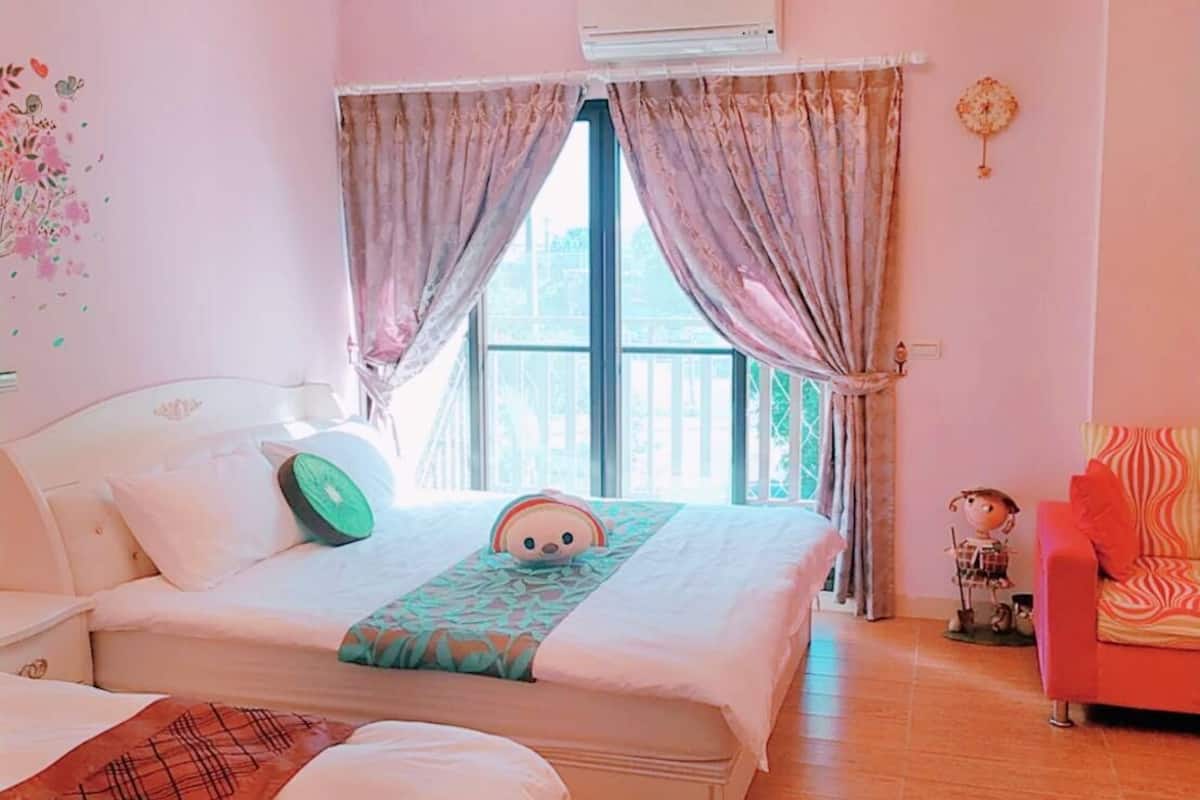A bedroom with a large bed, a sofa, an air conditioning unit, and a window with curtains.