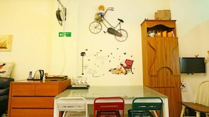 A room with a wooden cabinet, a desk with chairs, a wall-mounted TV, and a wall decoration of a bicycle and a bench. - Birds Flower B&B (Wujie)