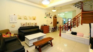 A living room with a black leather sofa, a white coffee table, and a wooden bench. There is a staircase with a wooden railing leading to an upper floor. - Birds Flower B&B (Wujie)