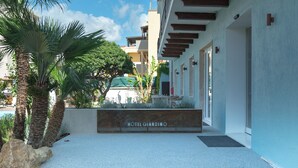Entrada de un hotel con letrero, palmeras y un edificio con balcones.