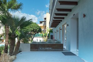 Entrada de un hotel con letrero, palmeras y un edificio con balcones.