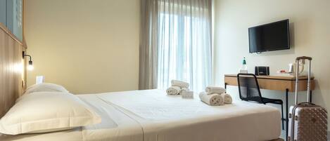 A hotel room with a bed, a desk, a chair, a television, and a suitcase.