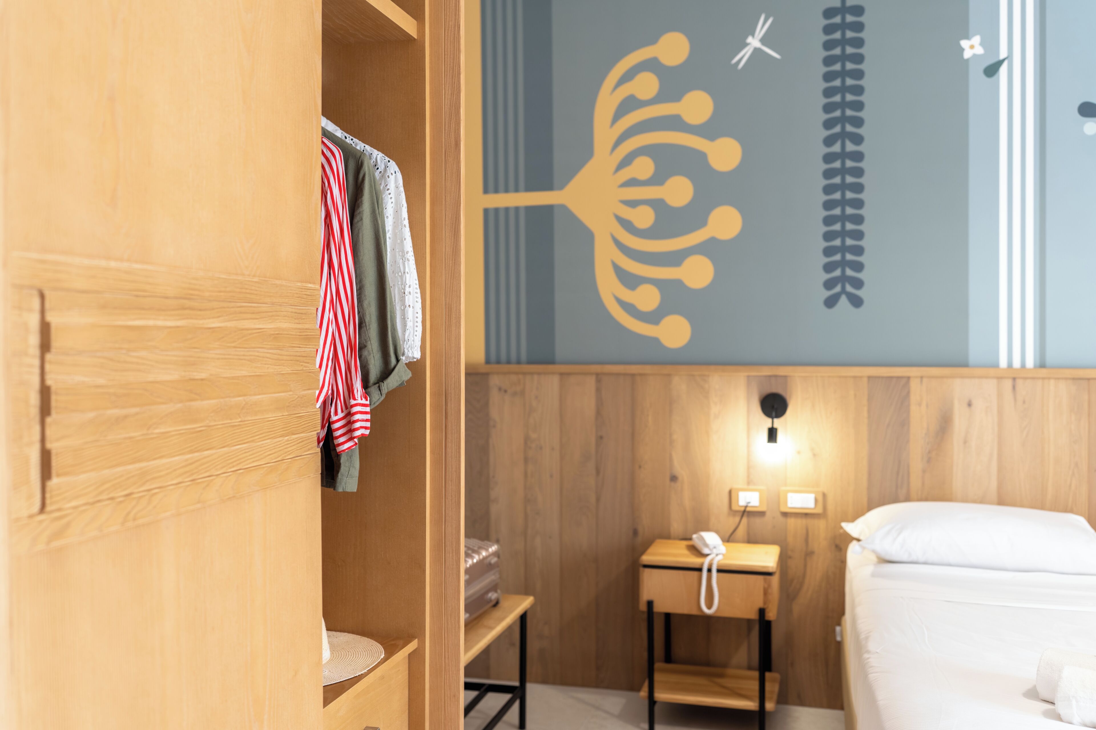 A hotel room with a wooden wardrobe, a small desk with a telephone, and a bed with white bedding.