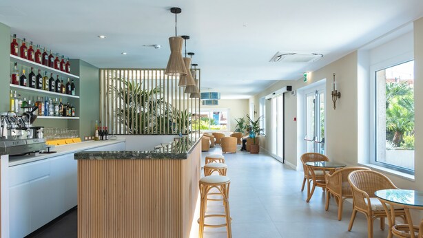 Un área de bar moderna con mostrador de madera, sillas de mimbre y vistas al exterior.