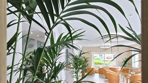 Amplio espacio interior con una disposición de asientos, plantas en macetas y una vista a través de una puerta.