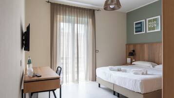 Una habitación de hotel con cama, escritorio con silla, televisor, botella de agua y cortina.