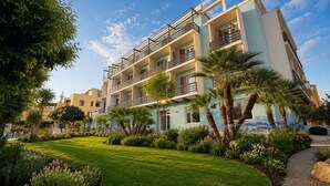 Un hotel de varios pisos con balcones, un jardín bien cuidado con palmeras y un cielo despejado.