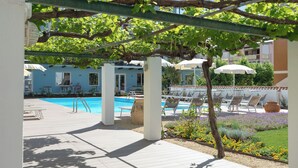 Zona de piscina con sillones de descanso, piscina y una pérgola cubierta de enredaderas.