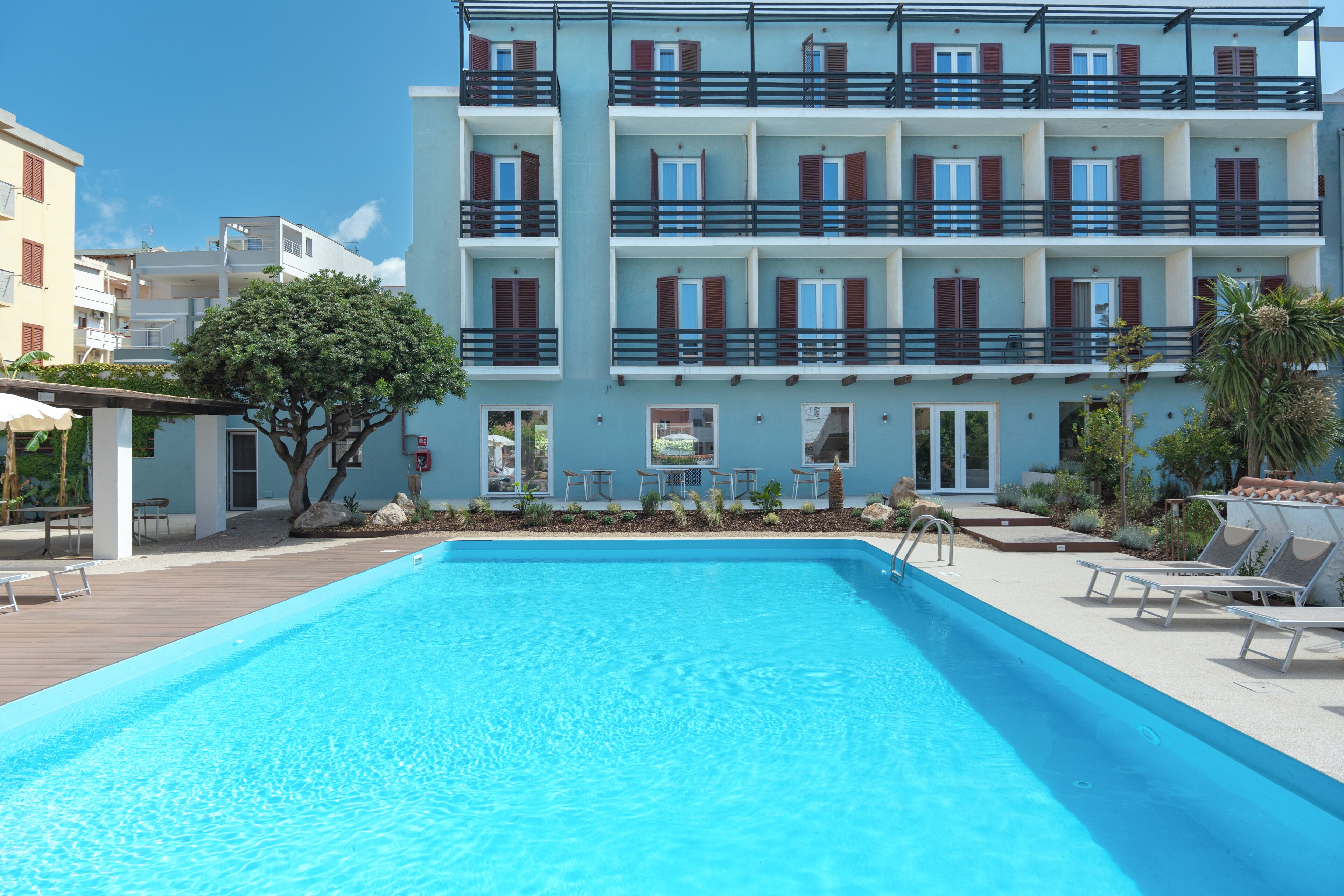 Una piscina con sillas de descanso, un edificio con balcones y un árbol.