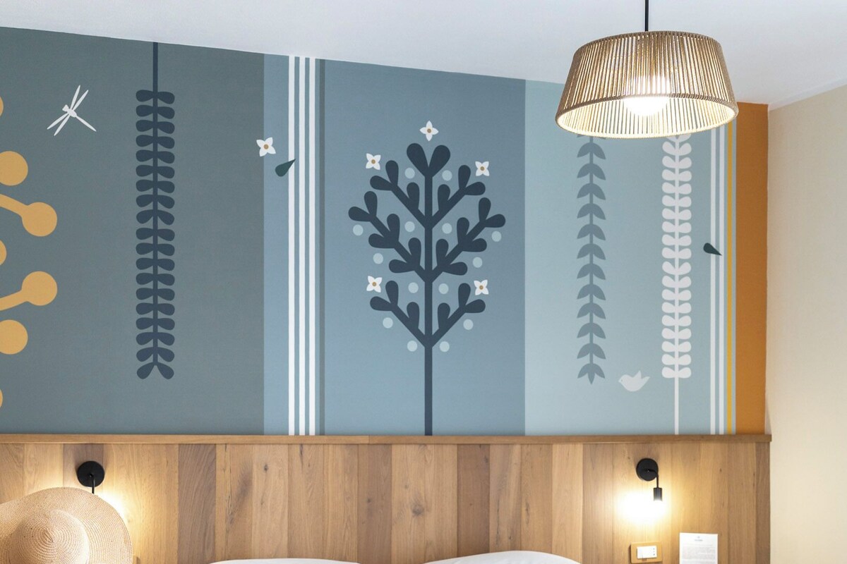 A hotel room with a bed, a suitcase, a wall with decorative elements, and a hanging light fixture.