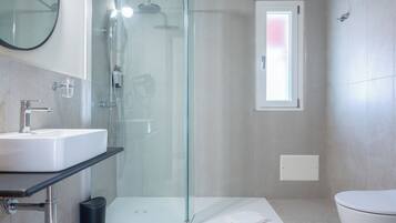 Een moderne badkamer met een douchecabine van glas, een wit wastafeltje en een toilet.