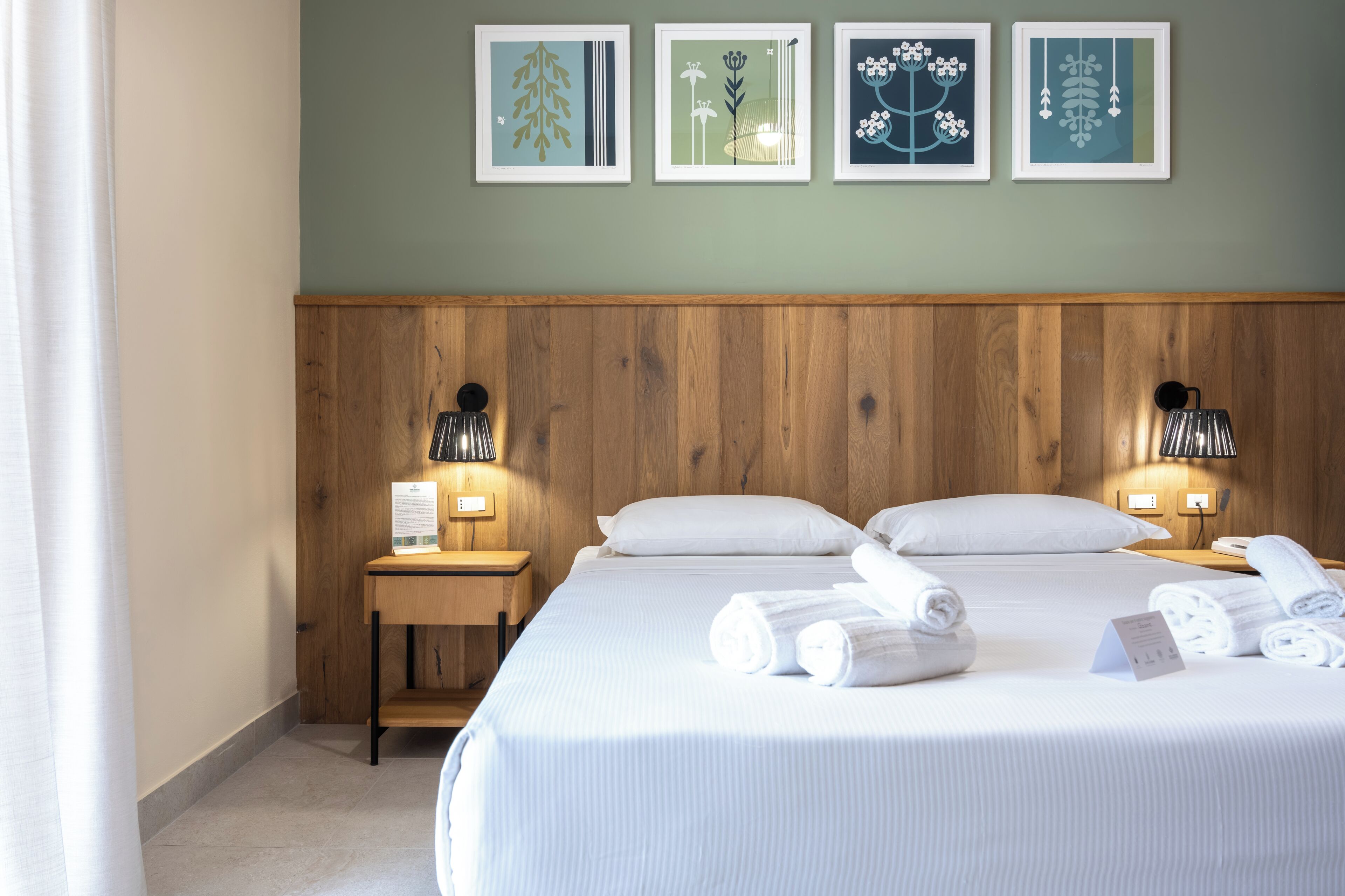 Ein Hotelzimmer mit einem hölzernen Kopfteil, einem Bett mit weißer Bettwäsche, zwei Nachttischen mit Lampen und gerahmten Bildern an der Wand.