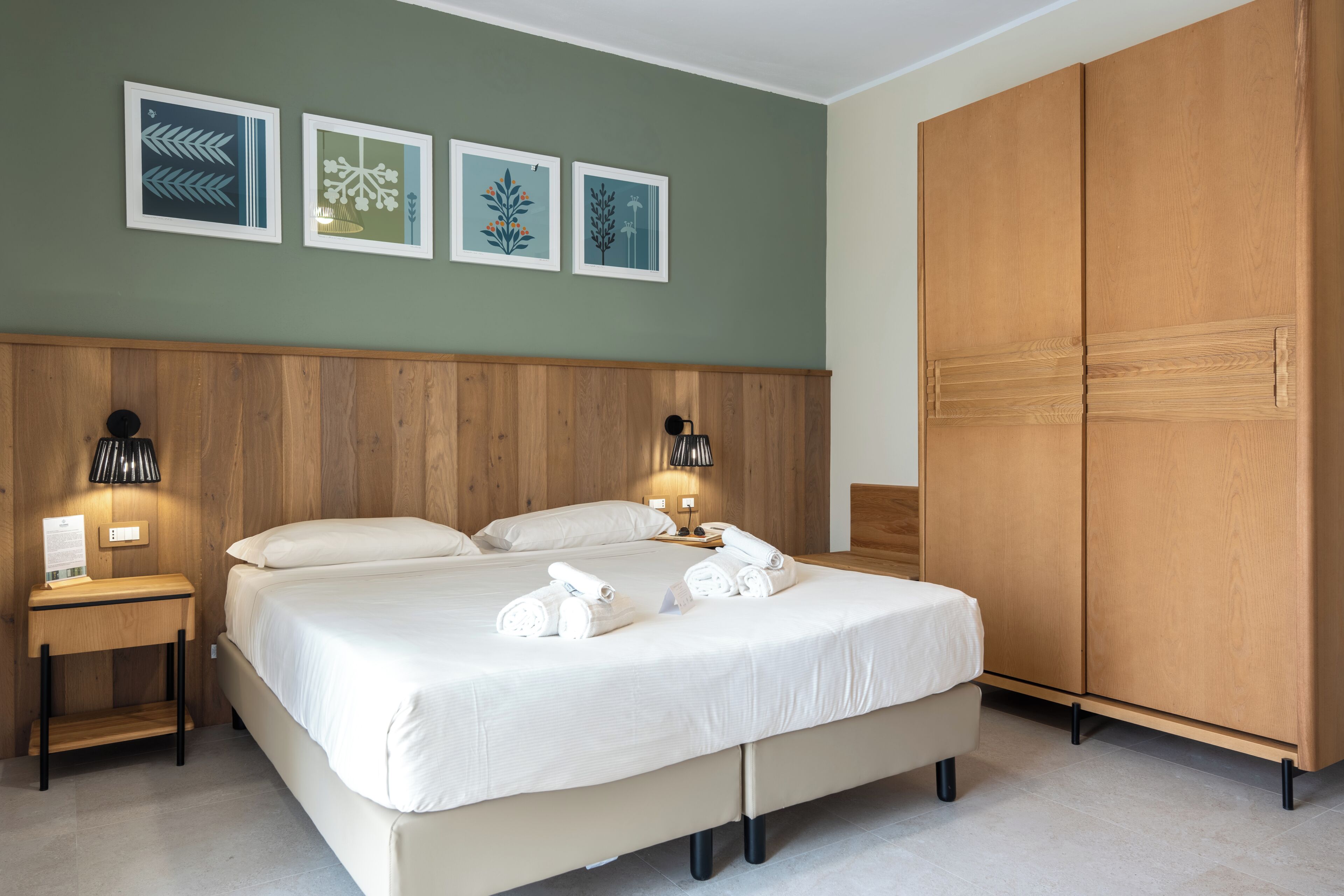 Un dormitorio con cabecera de madera, cama con ropa de cama blanca, dos lámparas de noche y un armario.