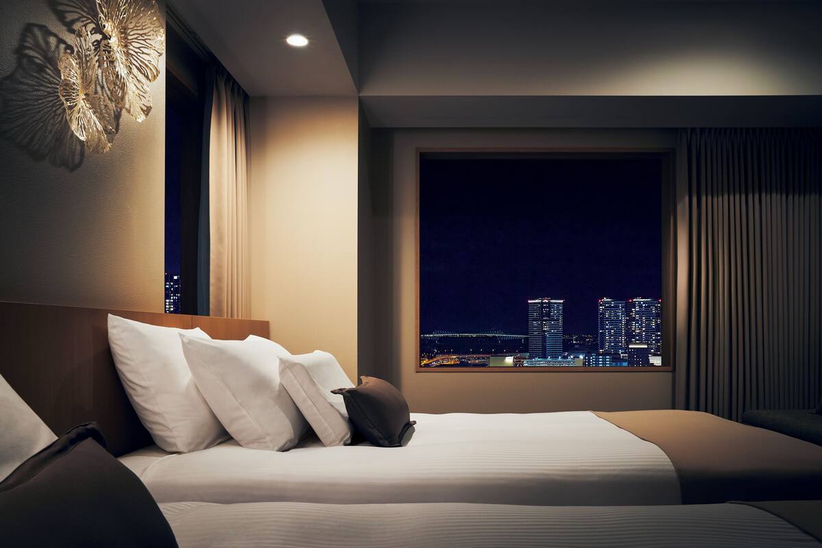 Een hotelkamer met een bed, uitzicht op een stadsbeeld 's nachts en een moderne kroonluchter.
