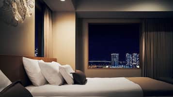 A hotel room with a bed, a view of a cityscape at night, and a modern light fixture.