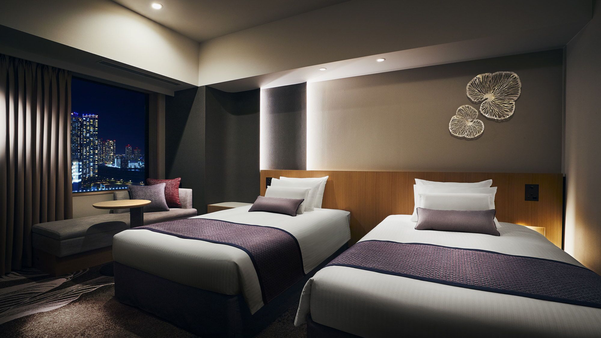 Une chambre d’hôtel avec deux lits, un canapé, une petite table et une vue sur la ville.