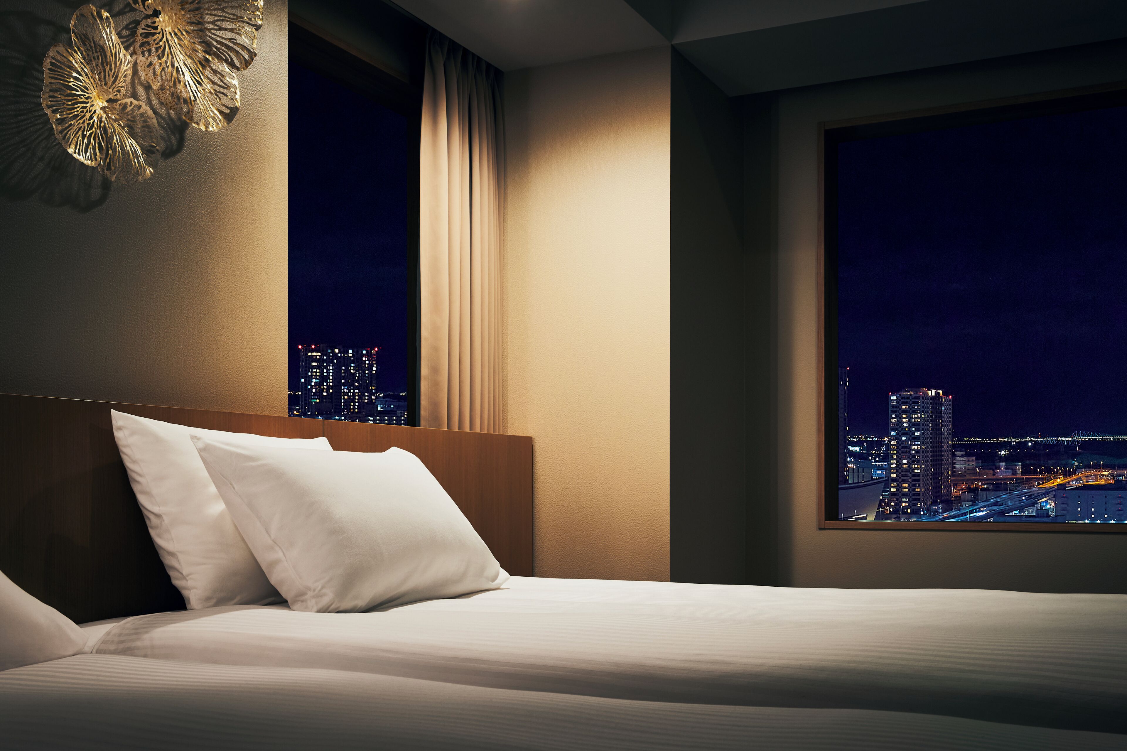 Une chambre d’hôtel avec un lit, une vue nocturne sur la ville et une grande fenêtre avec des rideaux.