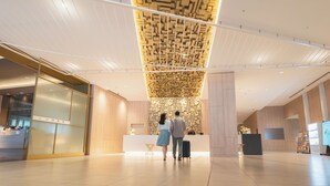 Een moderne hotellobby met een receptiebalie, een behanget plafond en een strak, minimalistisch design.