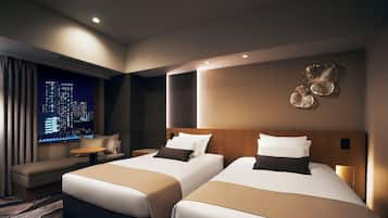 Habitación de hotel con dos camas, un sofá, una mesita y vistas a un paisaje urbano nocturno.