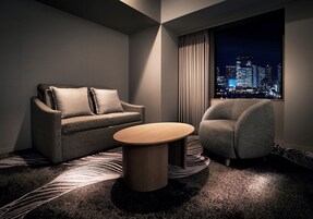 Ein modernes Hotelzimmer mit Sofa, Sessel und rundem Couchtisch.