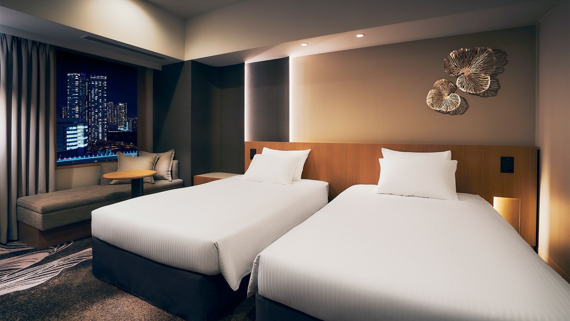 Une chambre d’hôtel avec deux lits, un canapé, une petite table et une vue sur la ville.