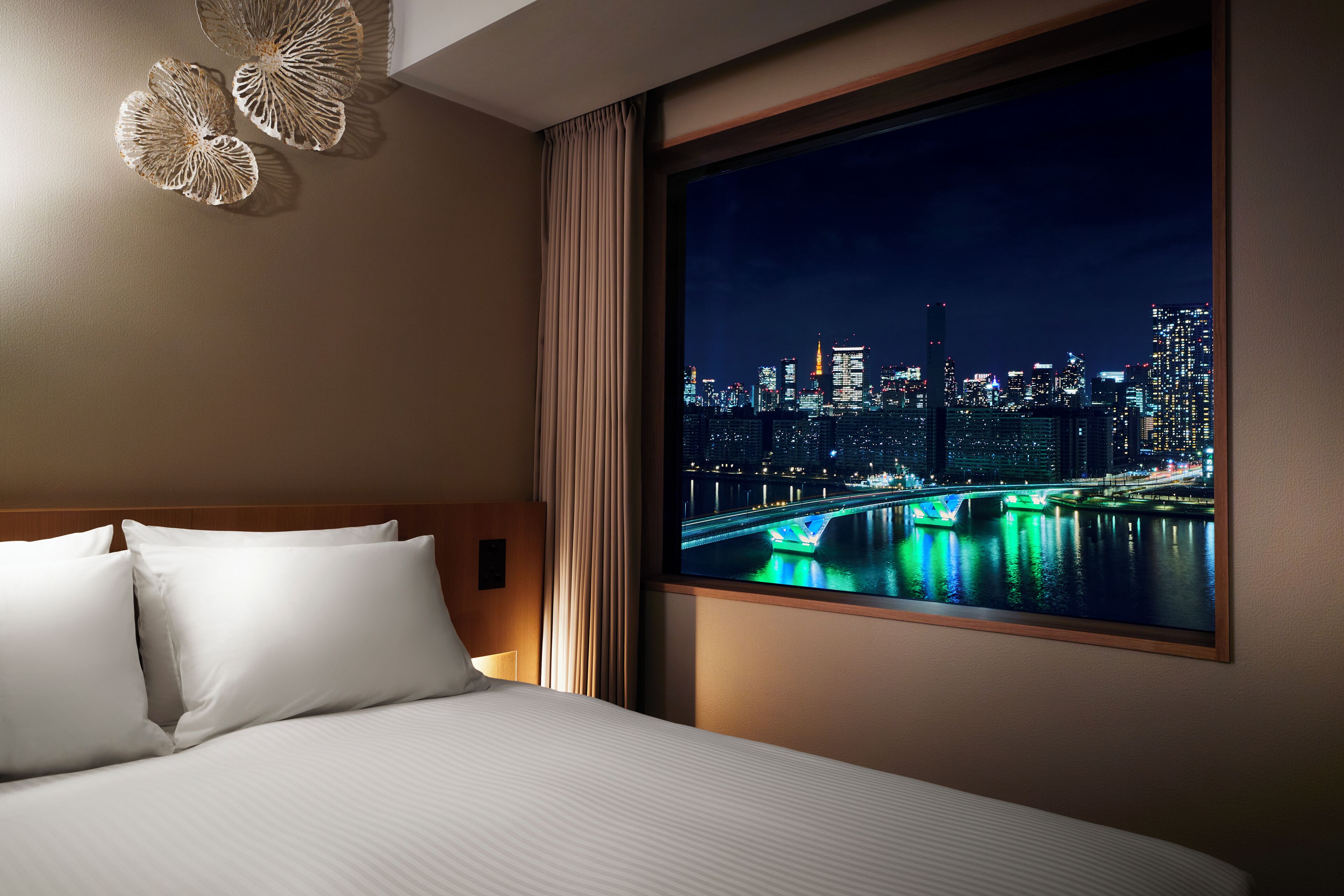 A hotel room with a large window, a bed with white linens, and a cityscape view at night.
