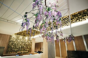Ein moderner Empfangsbereich mit geometrischer Wandgestaltung, einer Rezeption und hängenden violetten Blumen.