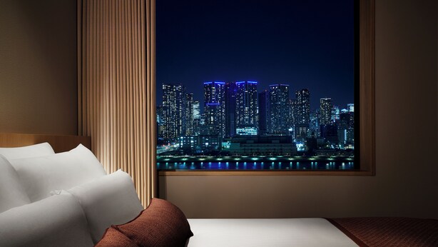 Een hotelkamer met een groot raam, een bed en uitzicht op een stadsbeeld 's nachts.