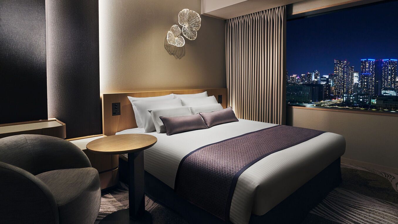 Une chambre d’hôtel avec un grand lit, une table ronde, une chaise, une vue sur la ville et un élément décoratif mural.