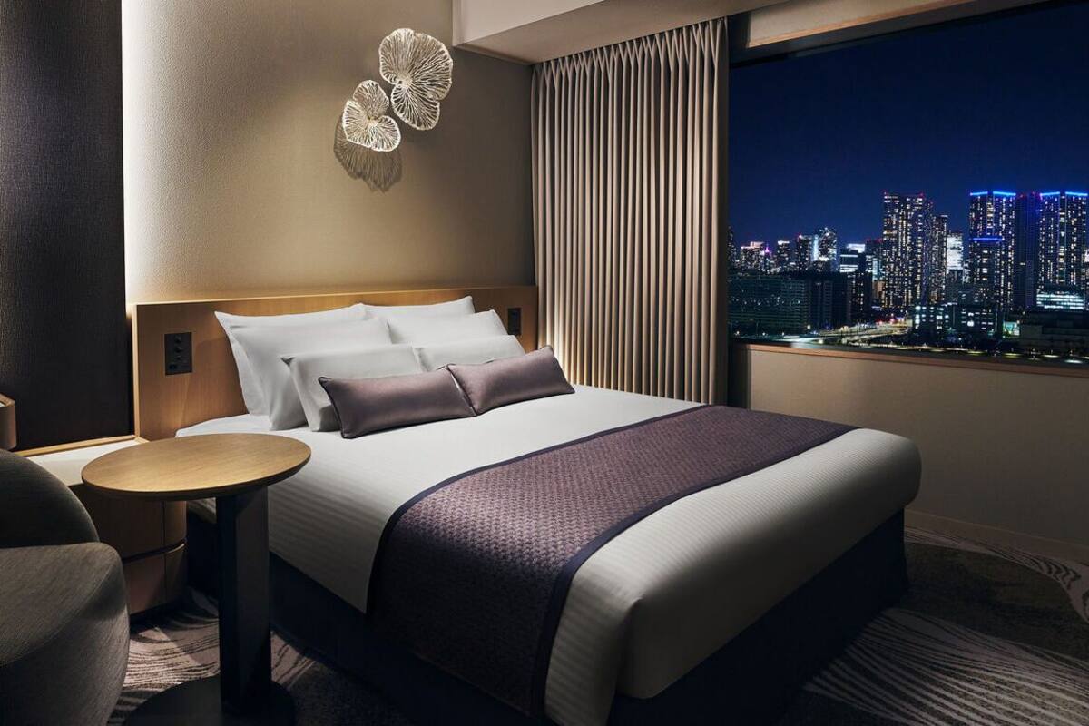 Hotelkamer met een groot bed, een ronde tafel, een stoel, stadszicht en een decoratief wandobject.