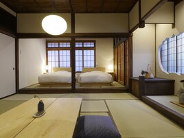 Una habitación tradicional japonesa con suelo de tatami, dos camas, una lámpara redonda grande en el techo y puertas correderas.