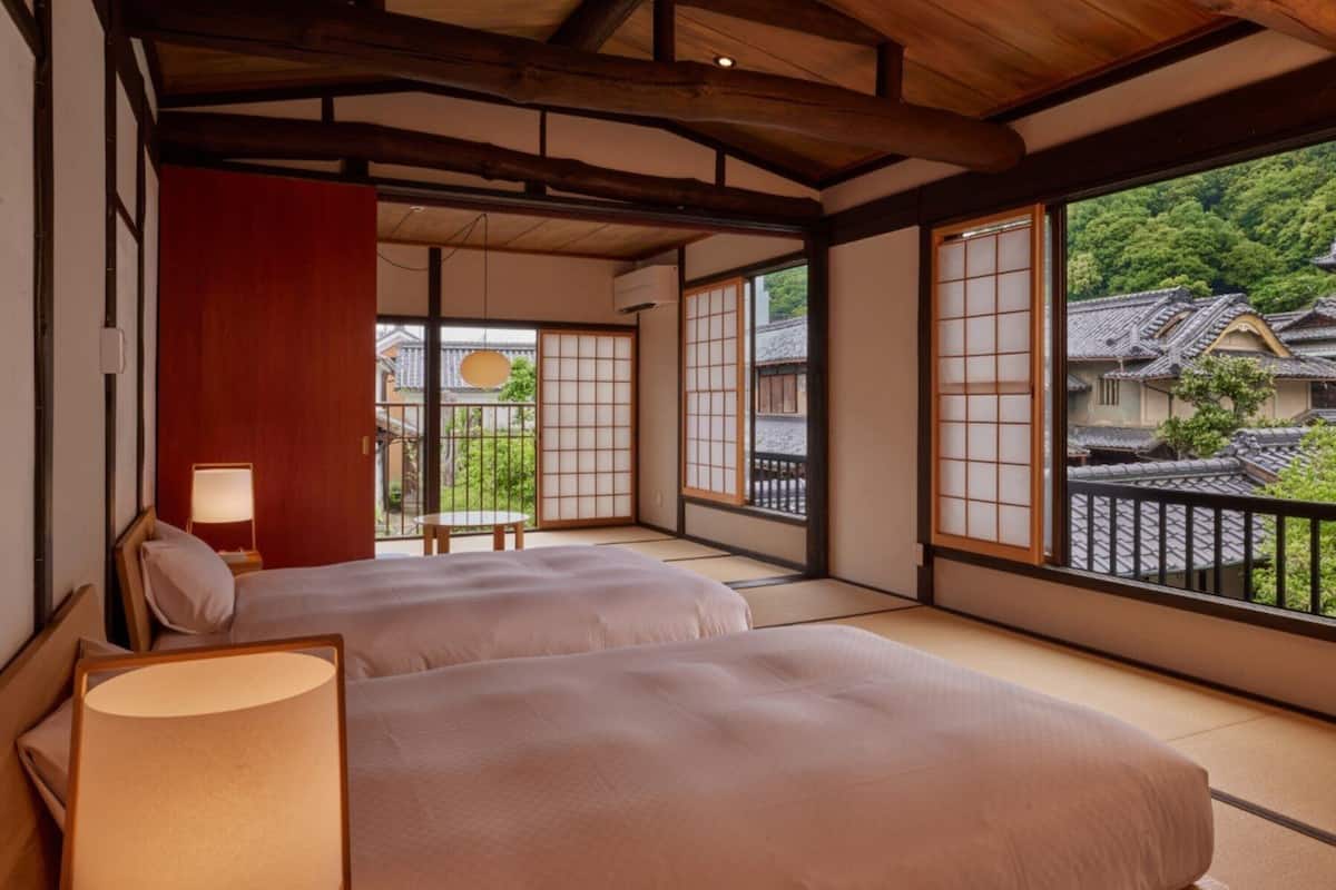 Una habitación japonesa tradicional con suelo de tatami, techo de madera bajo y puertas correderas que dan a un balcón.
