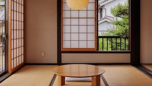 A traditional Japanese room with tatami flooring, a low wooden table, shoji screens, and a view of a residential area.