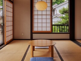 Una habitación japonesa tradicional con suelo de tatami, una mesa de madera baja, puertas correderas shoji y vista a una zona residencial.